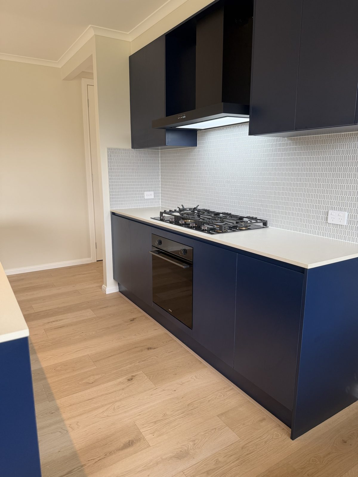 Timber-look laminate flooring through a new-build kitchen with navy cabinetry